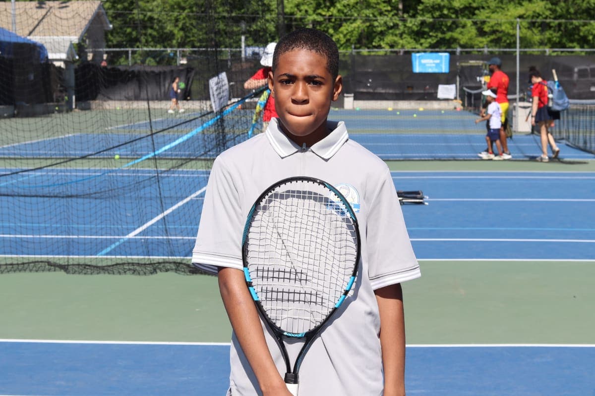 A young player holding a tennis racket on an outdoor court at a UnitedSets clinic