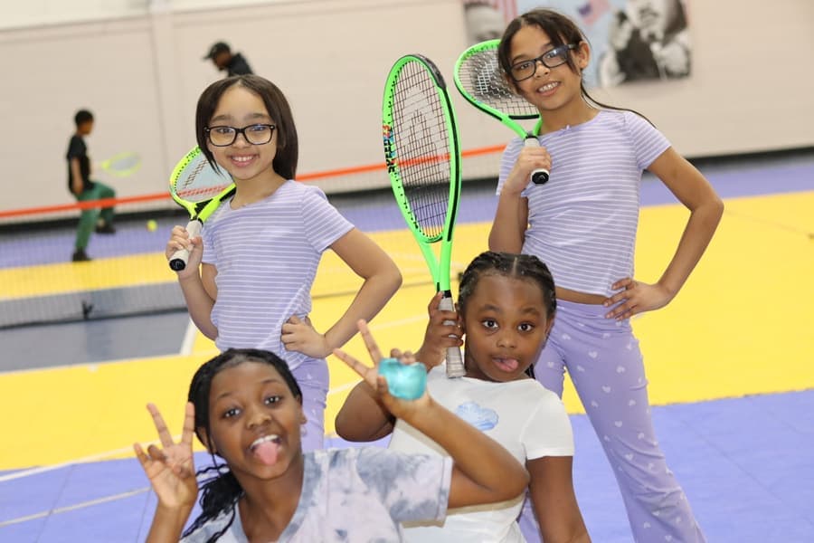 Four young players striking a pose with their rackets