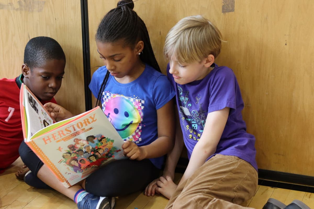 Three children reading a picture book together in the gym