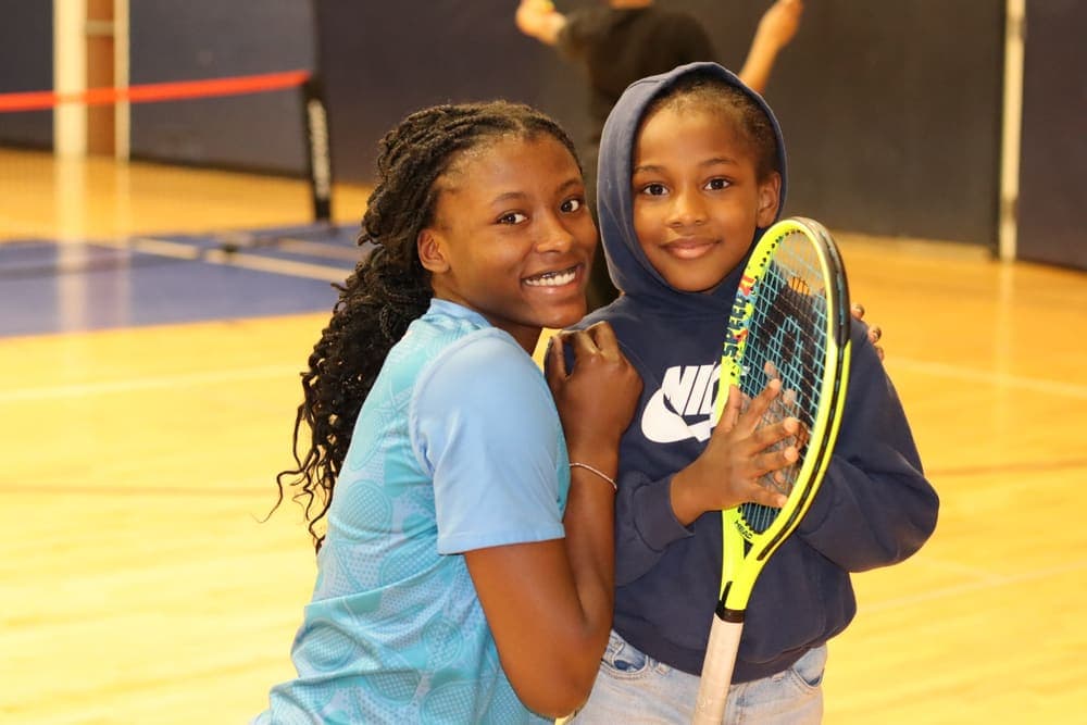 Two smiling students holding a tennis racket in the gym